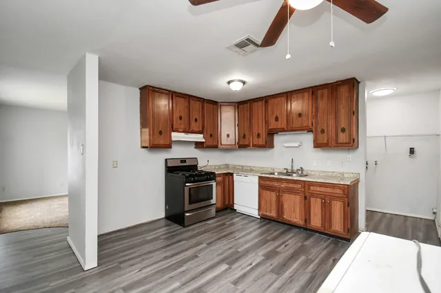 a kitchen with stainless steel appliances granite countertop wooden cabinets a refrigerator a stove a sink and a oven with wooden floor