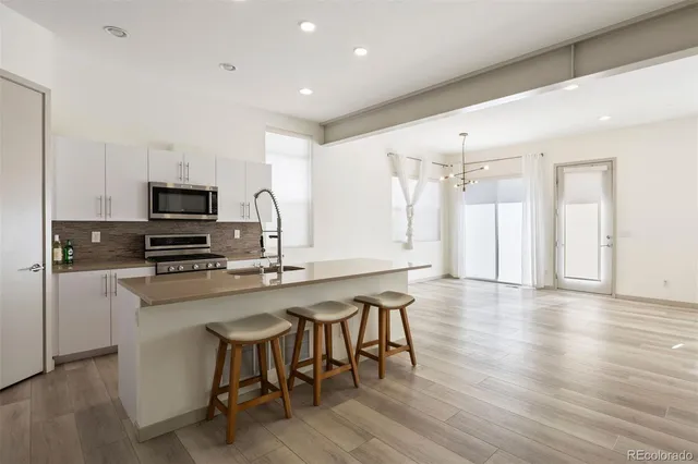 a kitchen with stainless steel appliances granite countertop a stove top oven a sink dishwasher a dining table and chairs with wooden floor