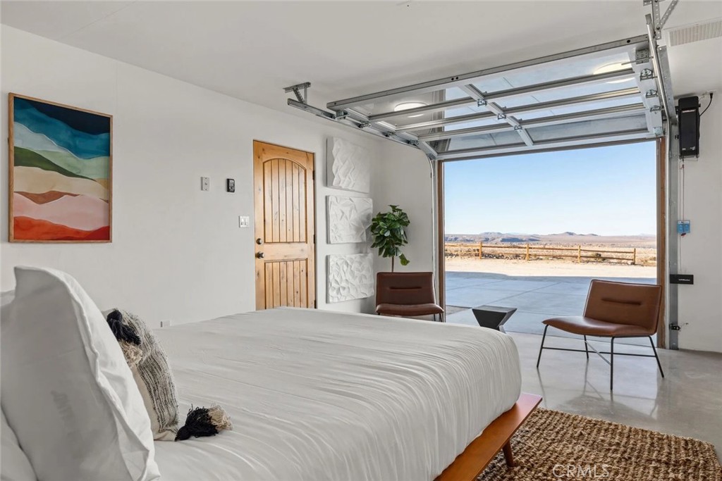 7030 Mile Square Road Joshua Tree, CA 92252 - Photo 42 of 58 a bedroom with a bed and a chair with the outer view