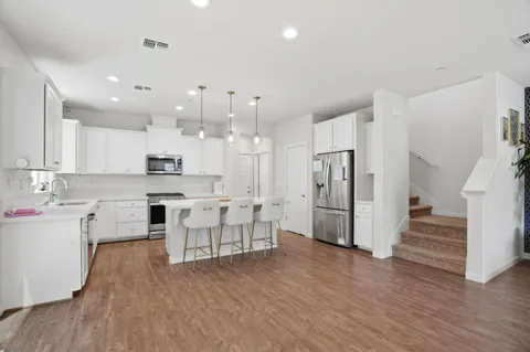 a kitchen with stainless steel appliances granite countertop a refrigerator a sink dishwasher a stove and white cabinets with wooden floor