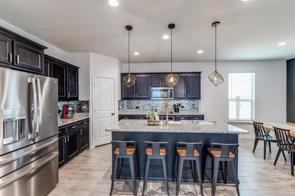 a kitchen with stainless steel appliances granite countertop a stove a refrigerator a kitchen island a table and chairs