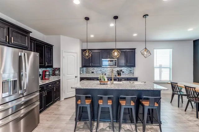 a kitchen with stainless steel appliances granite countertop a stove a refrigerator a kitchen island a table and chairs