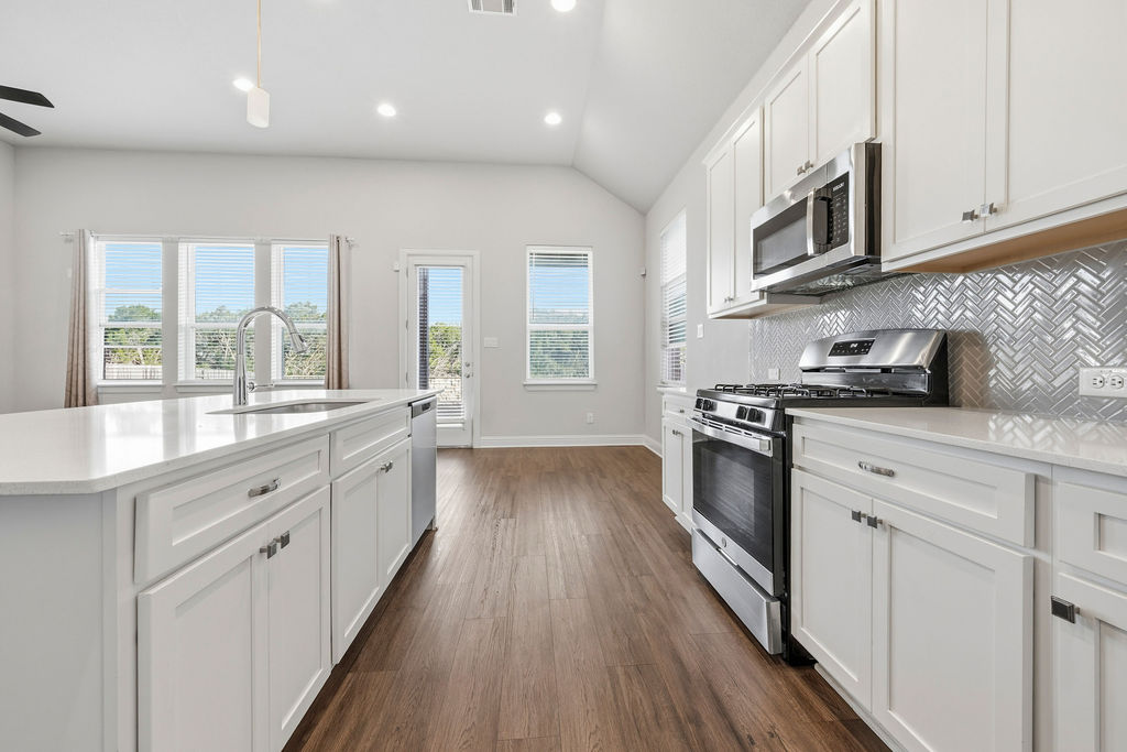 2032 Base Burner Path Leander, TX 78641 - Photo 3 of 34 Modern kitchen featuring white shaker cabinetry, stainless steel appliances, a herringbone tile backsplash, and wood-finish flooring