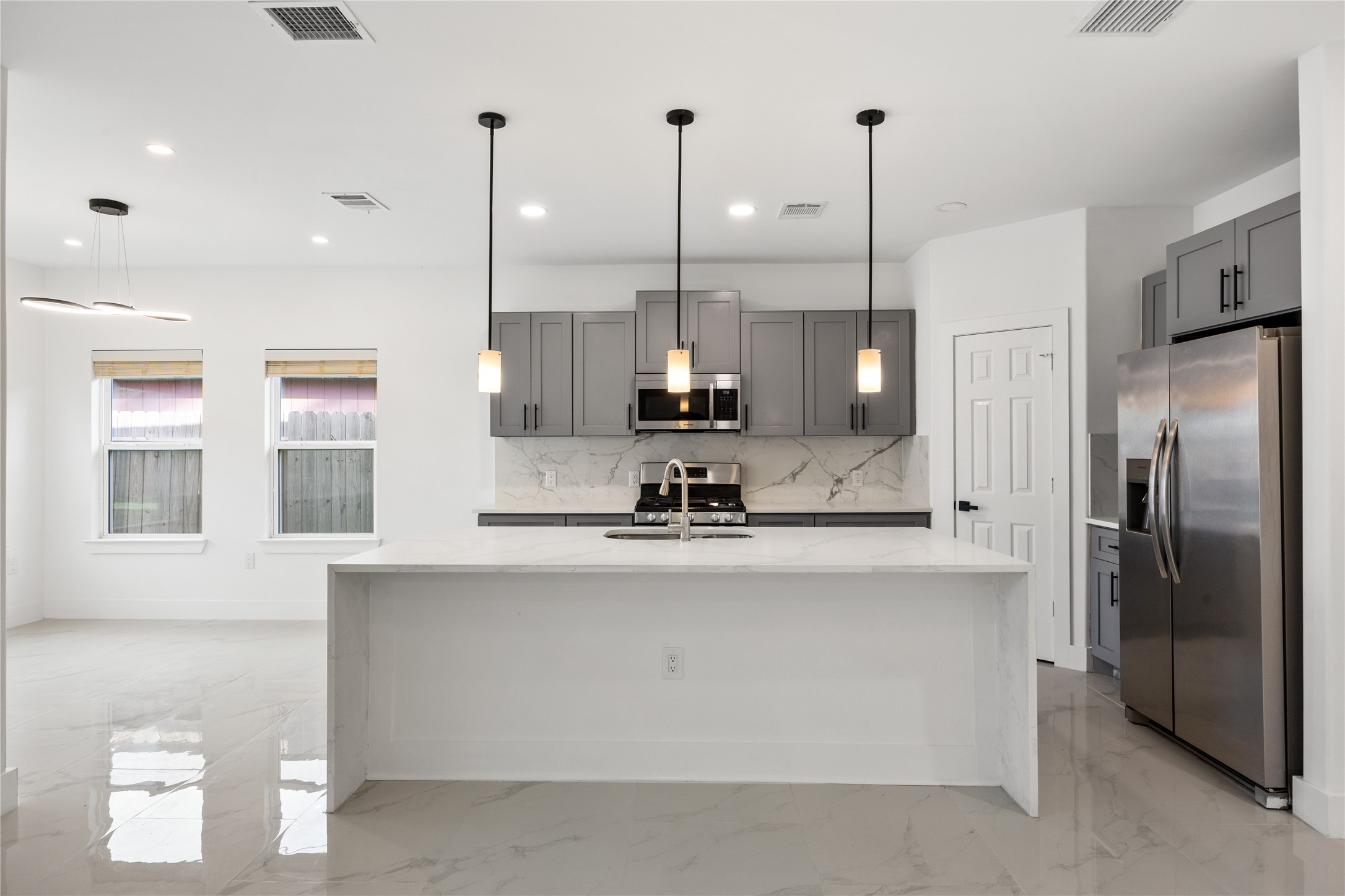 1121 Austin Street Rosenberg, TX 77471 - Photo 17 of 44 This modern kitchen features sleek gray cabinets, a large quartz island, stainless steel appliances, and chic pendant lighting, offering a bright and open space ideal for cooking and entertaining.