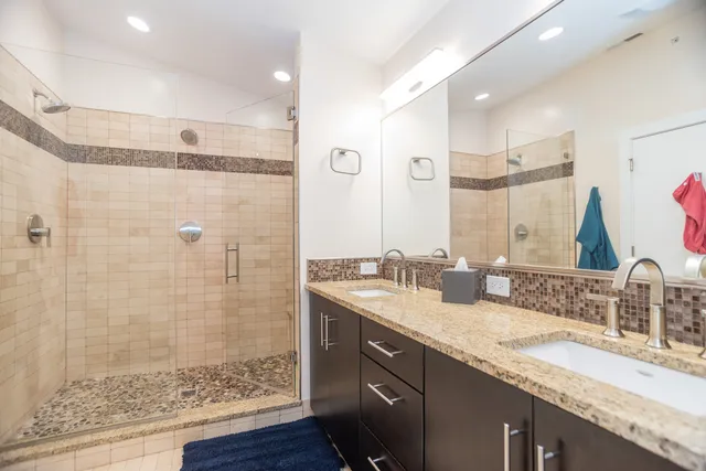 a bathroom with a granite countertop double vanity sink mirror and shower