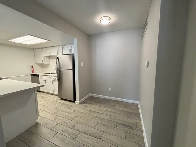 a view of a refrigerator in kitchen and an empty room with wooden floor