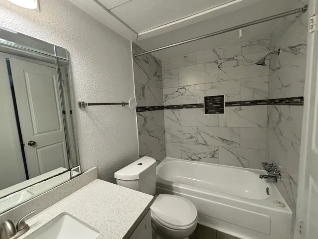 a bathroom with a granite countertop bathtub shower sink vanity and toilet