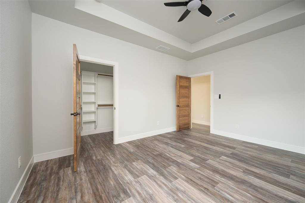 411 West Elm Street Whitewright, TX 75491 - Photo 13 of 31 Unfurnished bedroom featuring a raised ceiling, a walk in closet, wood finished floors, and a ceiling fan