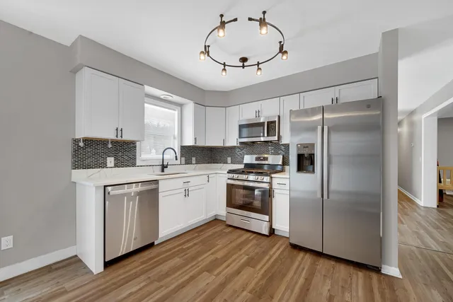 a kitchen with stainless steel appliances granite countertop a refrigerator a sink dishwasher a stove and white countertops with wooden floor