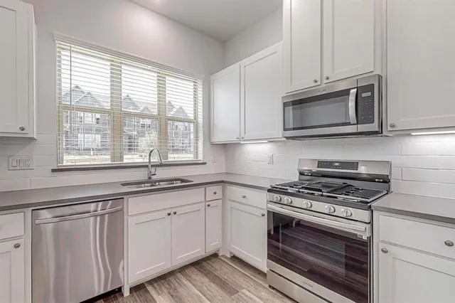 a kitchen with granite countertop white cabinets appliances and a window