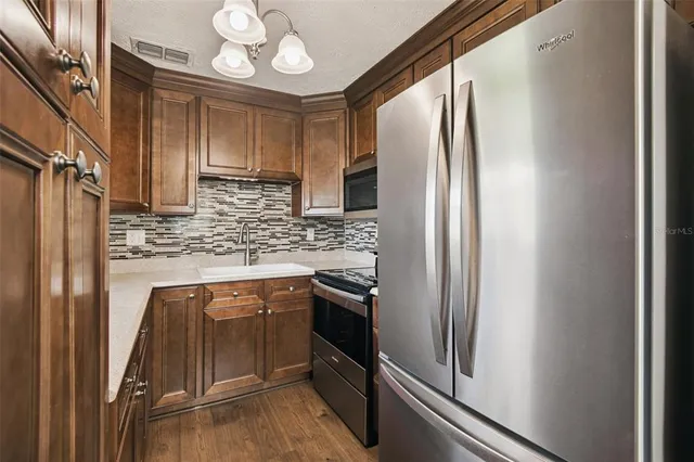 a kitchen with stainless steel appliances granite countertop a refrigerator a stove and a sink with wooden floor