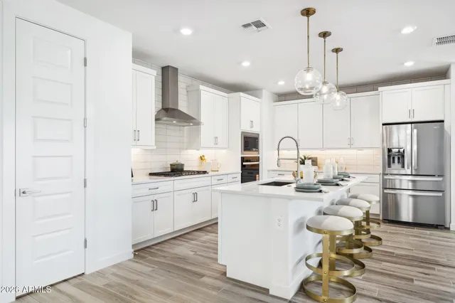 a kitchen with stainless steel appliances granite countertop a refrigerator a sink dishwasher a stove and white cabinets with wooden floor