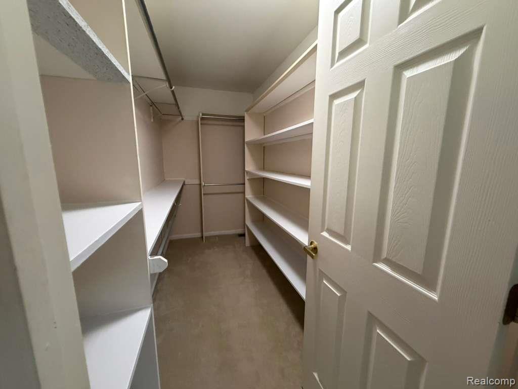 1154 Bluebird Drive Rochester, MI 48307 - Photo 26 of 34 Walk-in closet featuring extensive built-in shelving, hanging rods, and neutral-toned carpeting