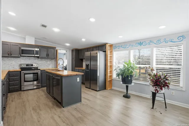 a kitchen with stainless steel appliances granite countertop a refrigerator a stove a sink a microwave and a dining table with wooden floor