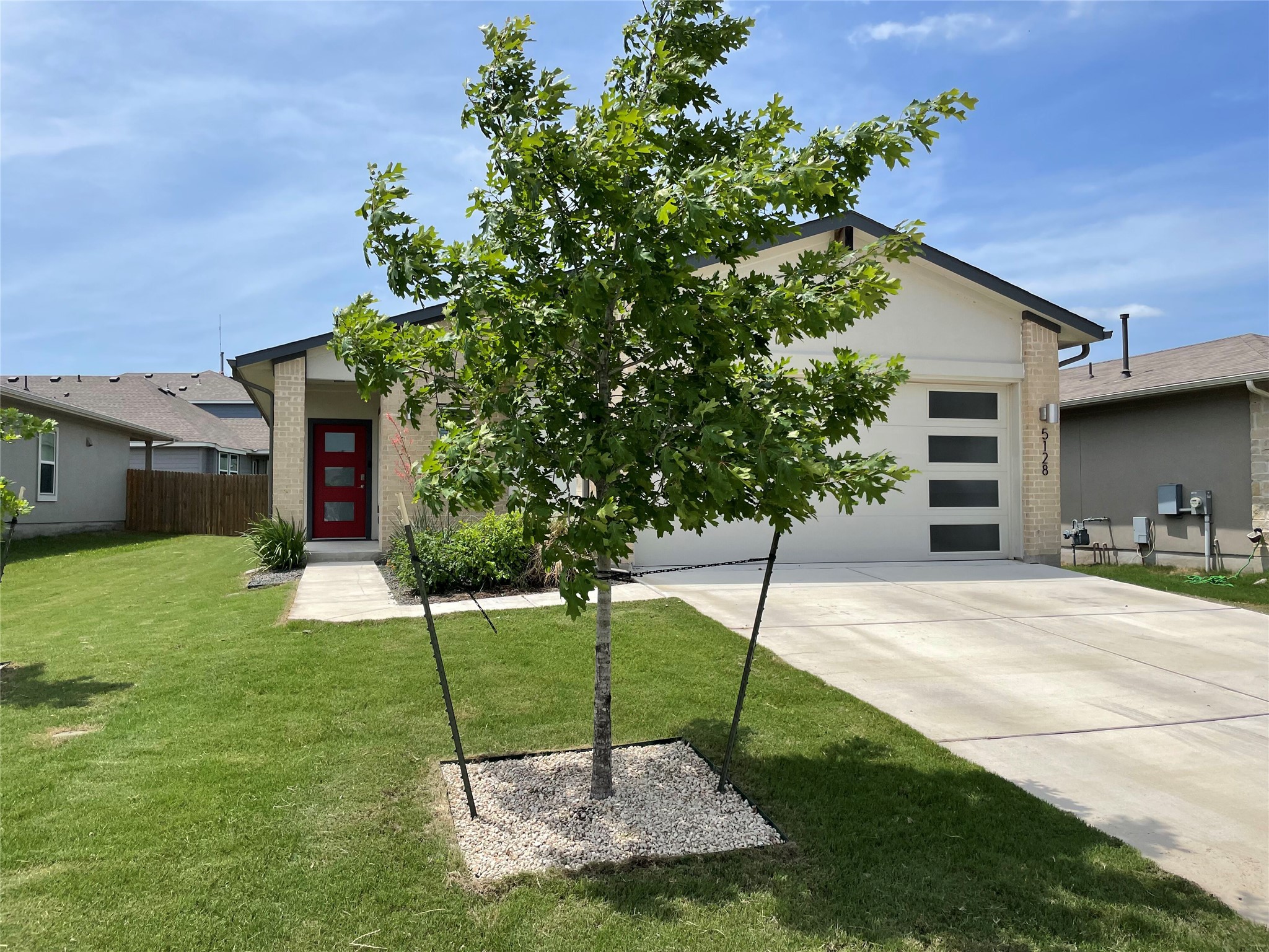 5128 Vanner Path Georgetown, TX 78626 - Photo 3 of 20 Contemporary single-story residence featuring a striking red entrance door, an attached garage with frosted glass panels, a concrete driveway, and a verdant lawn