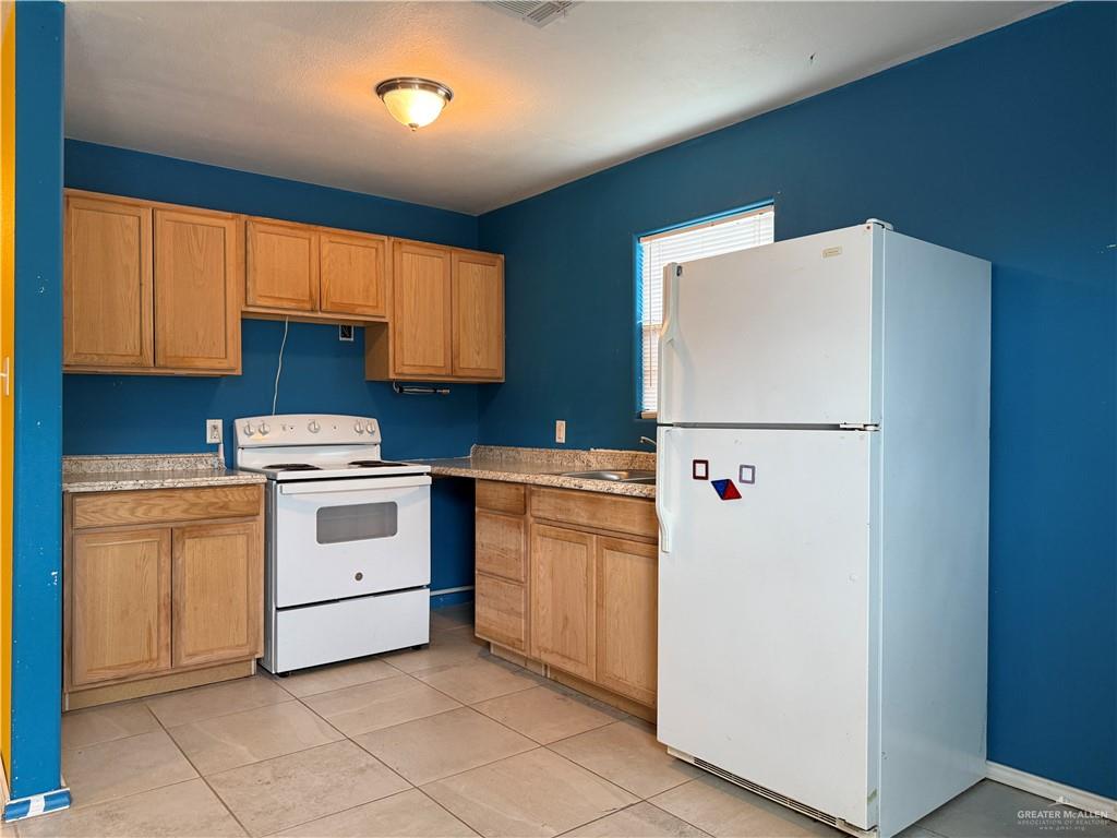 307 Hawaii Street Alton, TX 78573 - Photo 13 of 17 The kitchen features light-toned wooden cabinetry, a white stove, and a white refrigerator