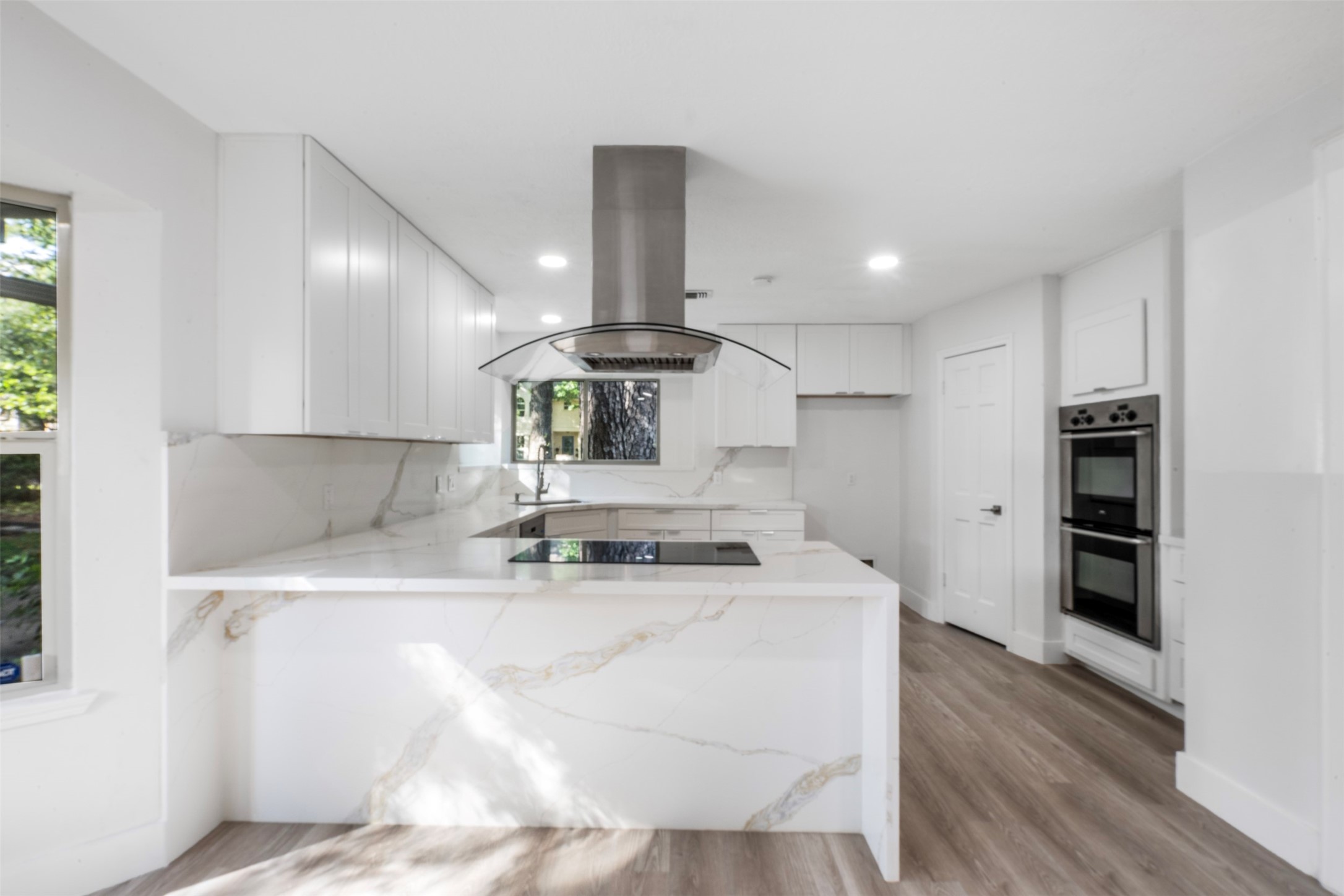 9543 Enstone Circle Spring, TX 77379 - Photo 9 of 50 This modern kitchen features sleek white cabinetry, marble countertops, and a central island with an integrated stovetop. It includes stainless steel appliances, a double oven, and hardwood flooring, offering a bright and contemporary space.