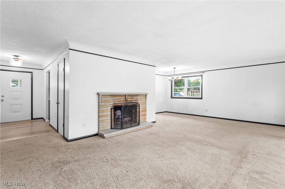 Unfurnished living room featuring carpet, a chandelier, and a stone fireplace