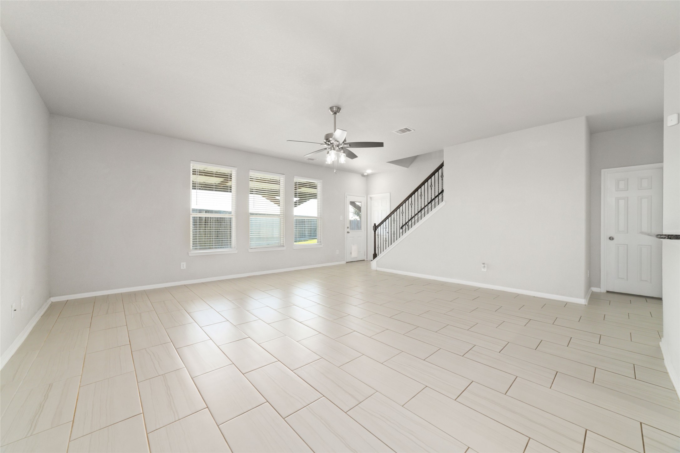 14838 Ruddy Duck Lane Houston, TX 77049 - Photo 4 of 33 Bright, spacious living area with neutral tile flooring, large windows for natural light, a ceiling fan, and a staircase with a modern railing.