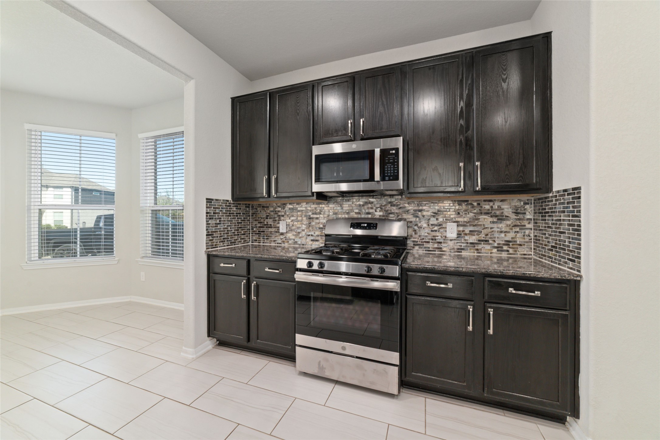14838 Ruddy Duck Lane Houston, TX 77049 - Photo 10 of 33 Modern kitchen with dark wood cabinetry, stainless steel appliances, and a stylish tile backsplash. The open layout includes large windows, providing ample natural light.