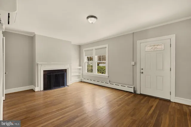 a view of an empty room with wooden floor fireplace and a window