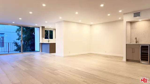 a view of an empty room with wooden floor and a kitchen