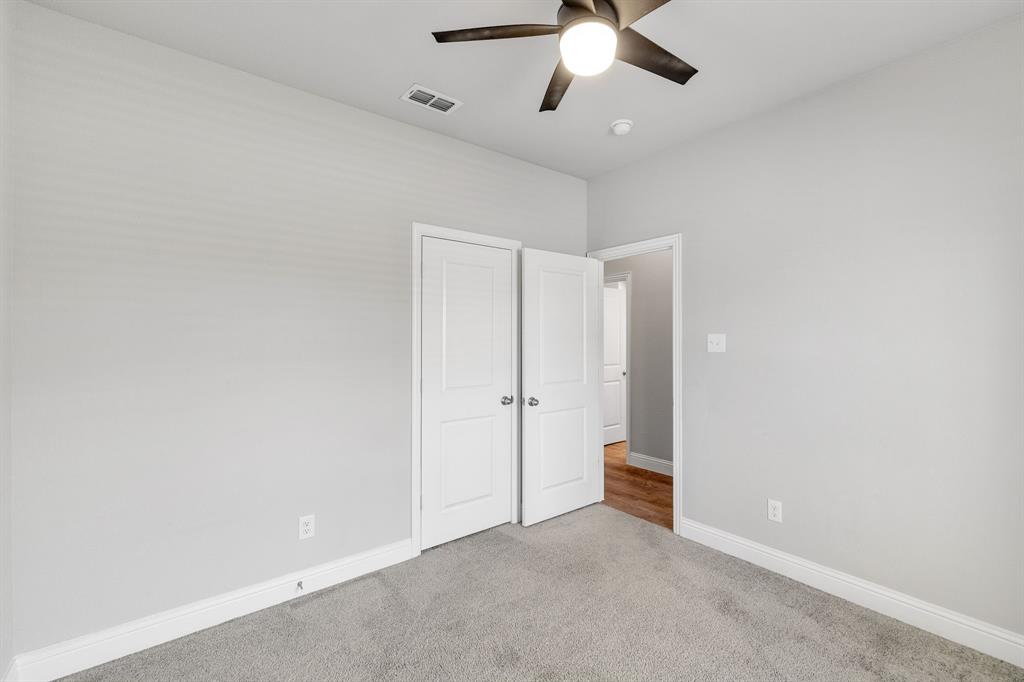 915 Timber Ridge Drive Justin, TX 76247 - Photo 31 of 39 Neutral gray walls with white trim, gray carpeting, a dark-toned ceiling fan with integrated lighting, and a bi-fold closet door