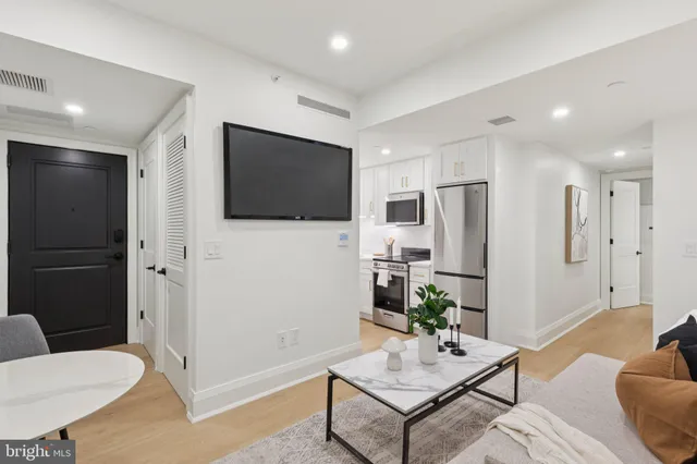 a living room with stainless steel appliances furniture a flat screen tv and a view of kitchen