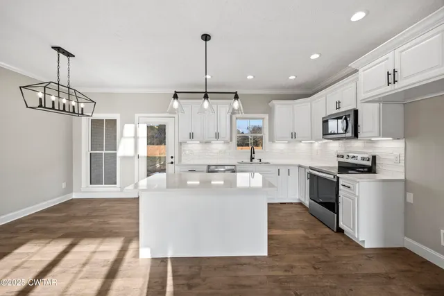 a large kitchen with stainless steel appliances granite countertop a stove a sink dishwasher a refrigerator and white cabinets with wooden floor