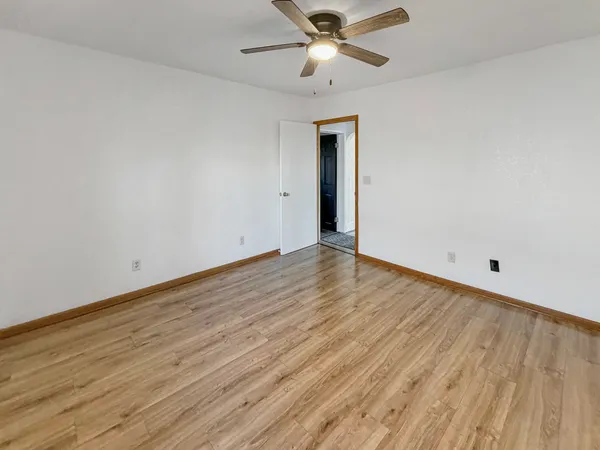 a view of an empty room with wooden floor and a ceiling fan