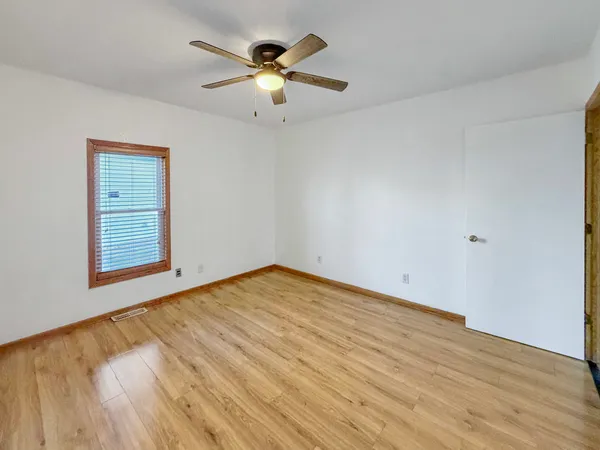 an empty room with wooden floor chandelier fan and windows