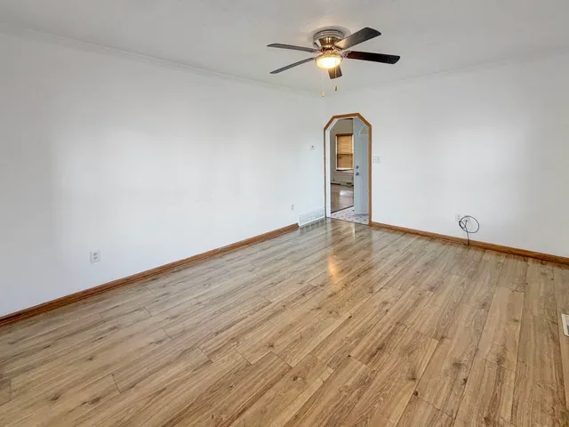 an empty room with wooden floor ceiling fan and window