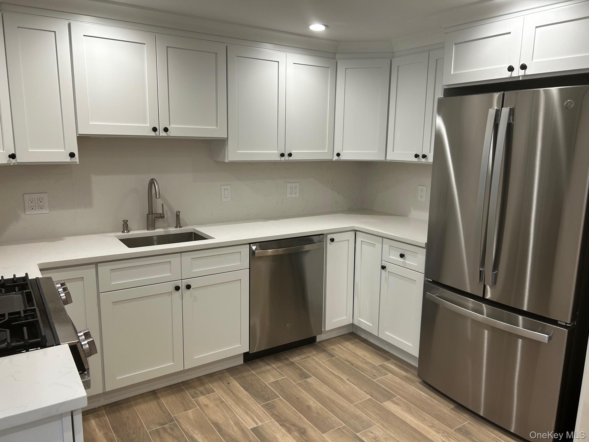 65 Linwood Road North, Unit GARDEN Port Washington, NY 11050 - Photo 5 of 11 Kitchen with appliances with stainless steel finishes, white cabinets, wood tiled floors, and light stone countertops