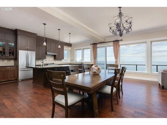 a kitchen with stainless steel appliances granite countertop a refrigerator a sink dishwasher a stove and a dining table with wooden floor