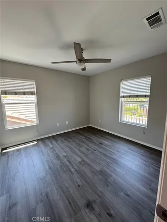 an empty room with wooden floor a ceiling fan and windows