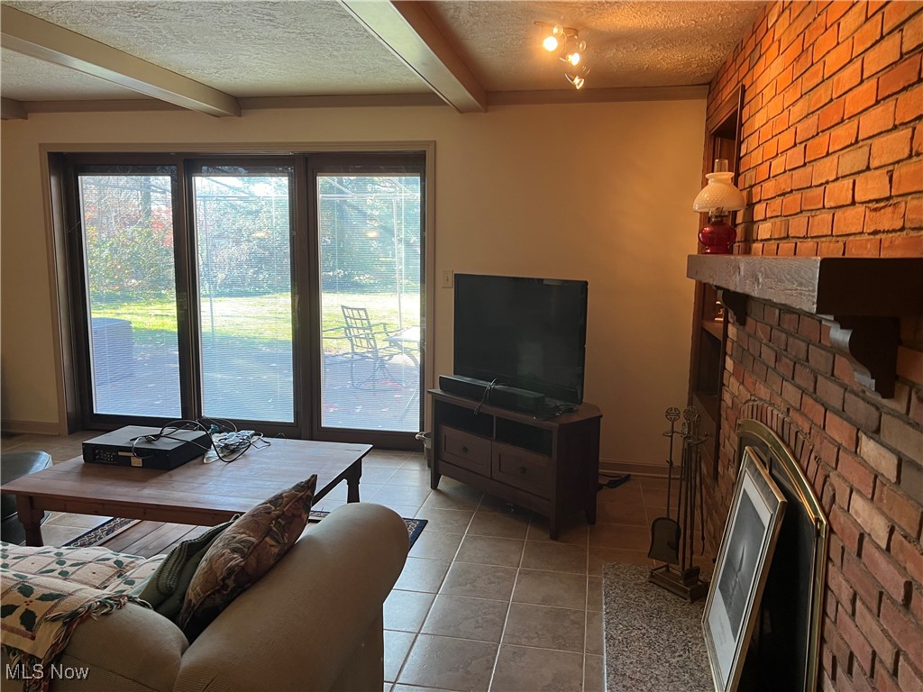 3330 Stanley Road Akron, OH 44333 - Photo 11 of 22 Living room featuring brick wall, a textured ceiling, beam ceiling, light tile patterned floors, and a fireplace