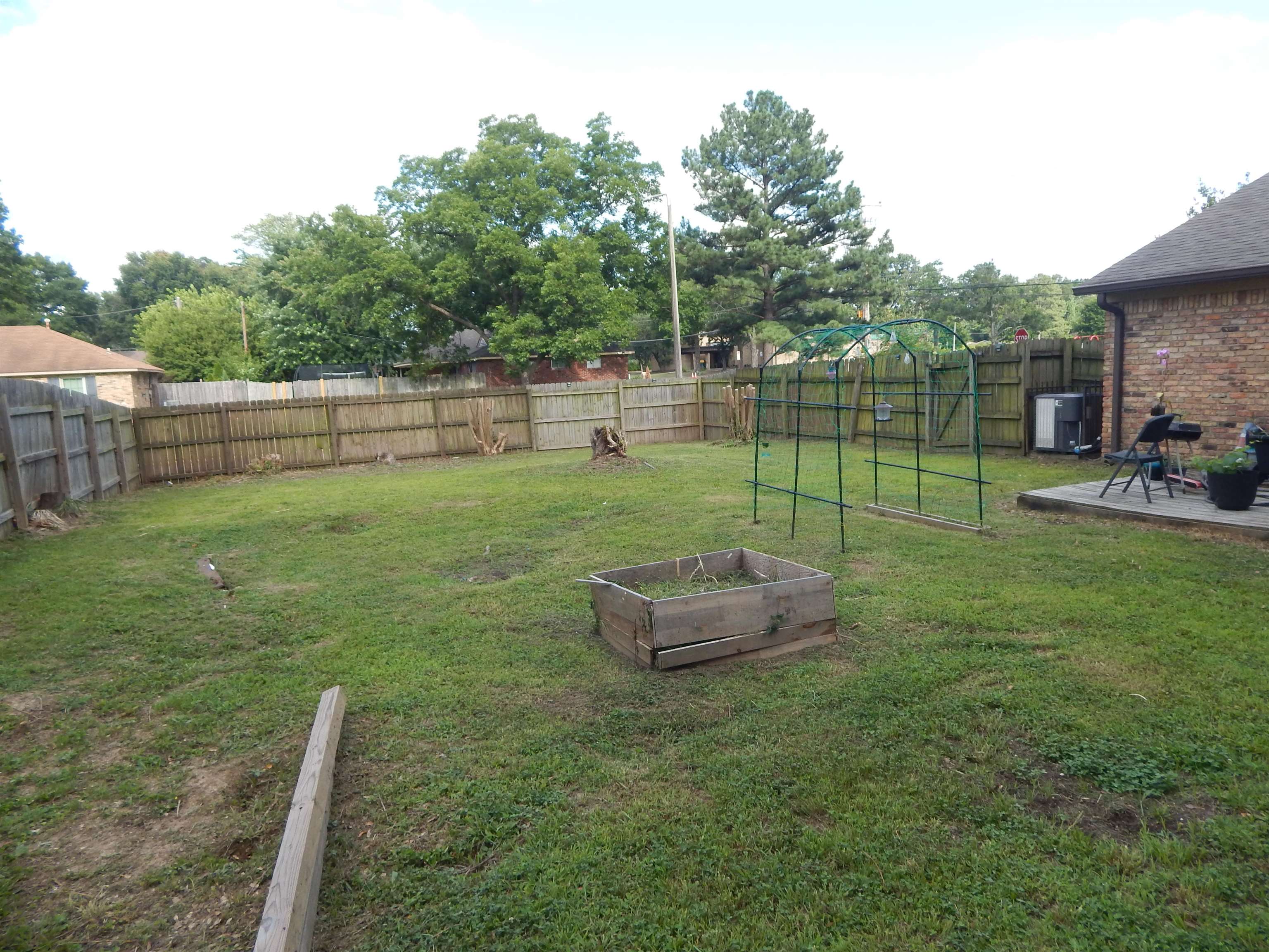 4956 Cottonwood Road Memphis, TN 38118 - Photo 3 of 13 Spacious backyard featuring a wood privacy fence, concrete patio, and mature trees beyond the fence line