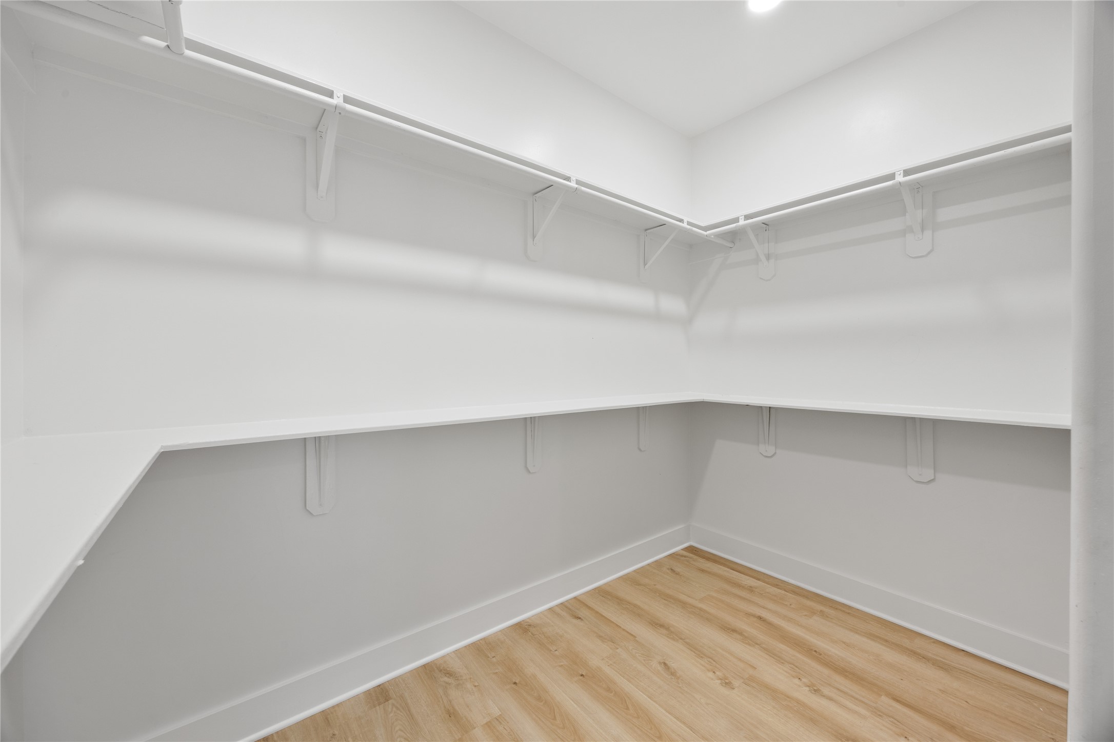 1121 Austin Street Rosenberg, TX 77471 - Photo 32 of 44 This photo shows a spacious walk-in closet with white shelving and hanging rods, complemented by light luxury vinyl and bright overhead lighting.