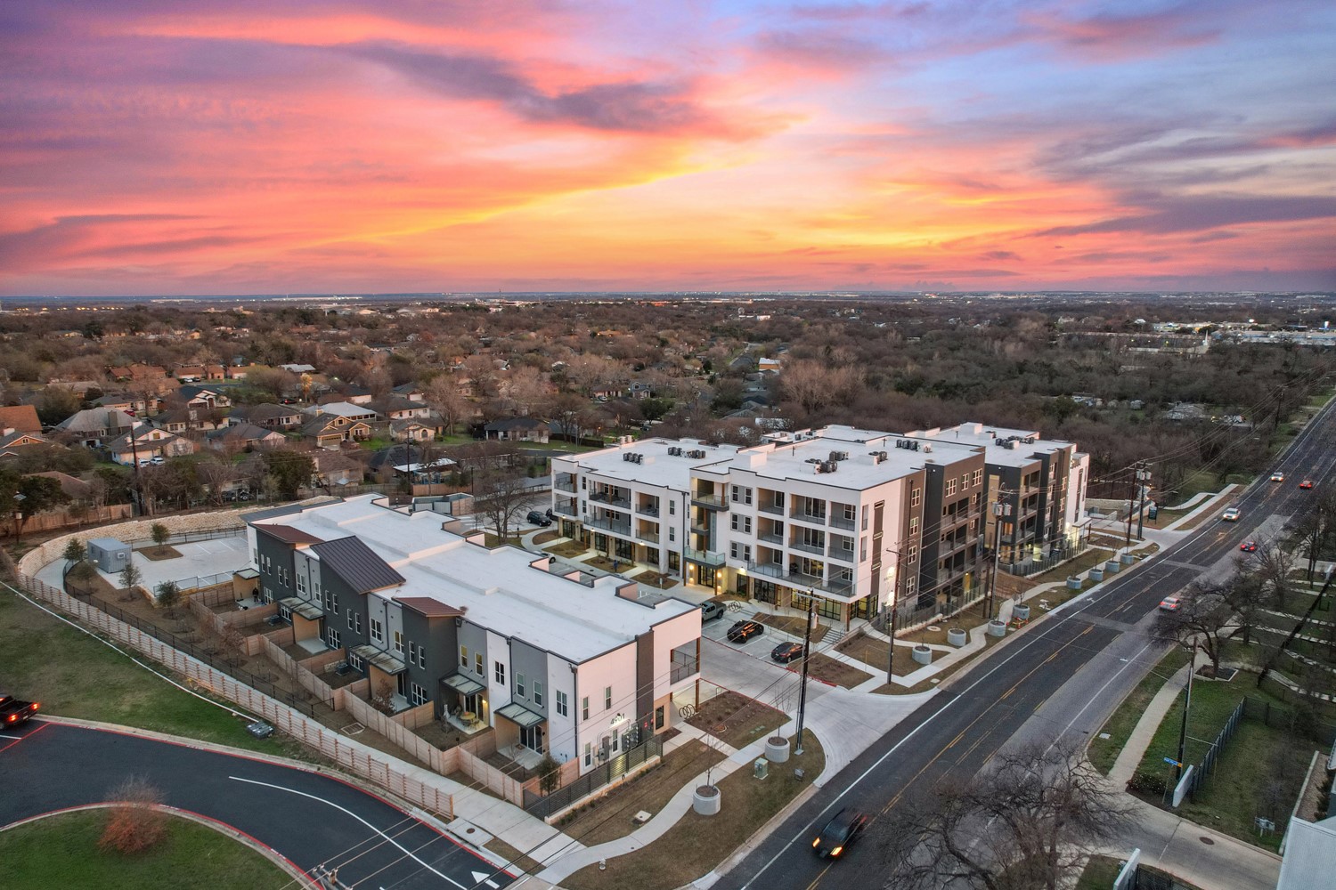 4901 Springdale Road, Unit 2308 Austin, TX 78723 - Photo 1 of 19 An aerial panorama capturing modern architecture against a vibrant sunset and extensive suburban greenery.