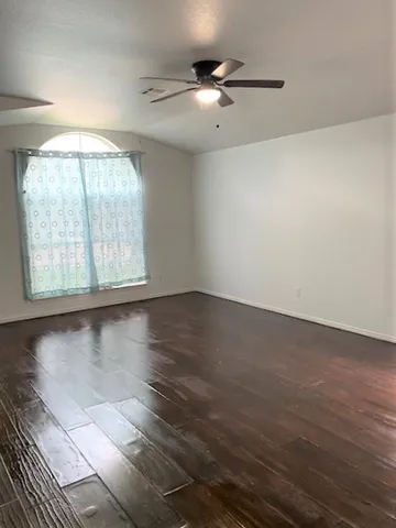 an empty room with wooden floor fan and windows