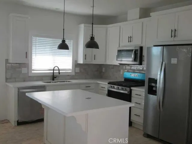 a kitchen with stainless steel appliances a sink a stove a refrigerator a center island and cabinets