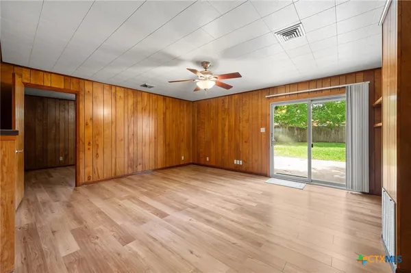 an empty room with windows a ceiling fan and wooden floor