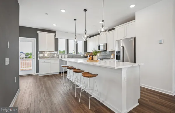 a kitchen with stainless steel appliances granite countertop a refrigerator a oven a sink and white cabinets with wooden floor