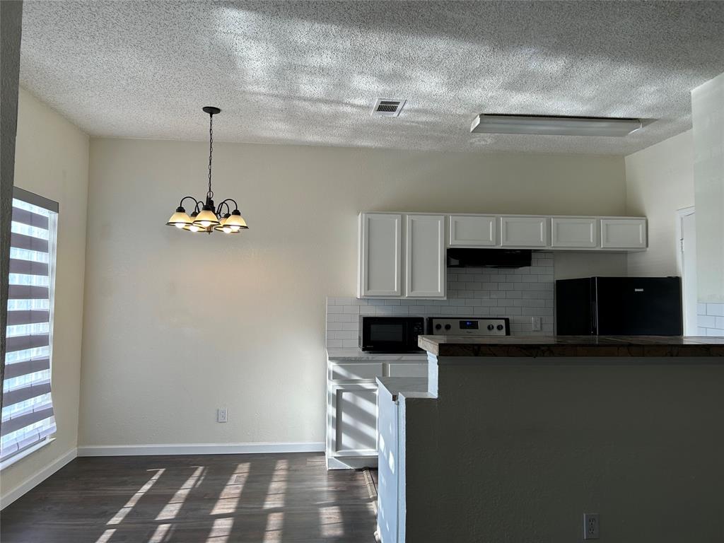 4107 Esters Road Irving, TX 75038 - Photo 13 of 21 Open-concept kitchen and dining area featuring white cabinetry, subway tile backsplash, dark wood-finish flooring, and a contemporary chandelier