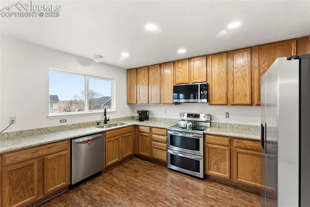 a kitchen with stainless steel appliances granite countertop wooden cabinets a sink a stove a refrigerator with grey cabinets and wooden floor