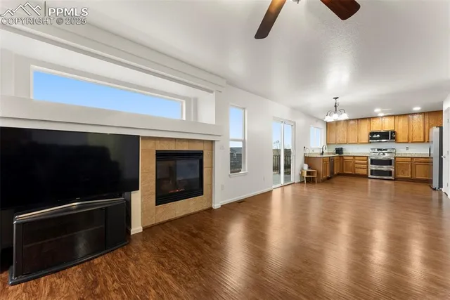 a view of an empty room and kitchen with fireplace wooden floor