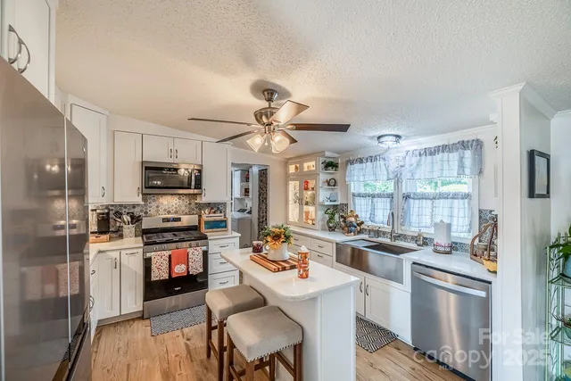 a kitchen with stainless steel appliances a stove a sink dishwasher a refrigerator white cabinets and wooden floor