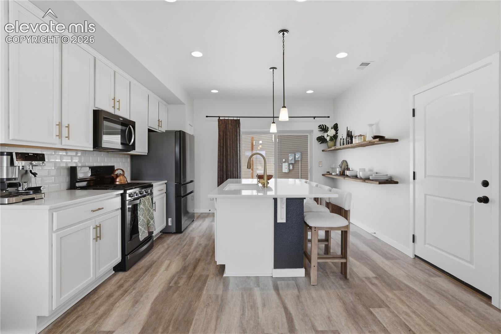 6008 Ashmore Road Colorado Springs, CO 80927 - Photo 11 of 48 Modern kitchen with white cabinetry and gold-tone hardware, featuring a white subway tile backsplash and black appliances