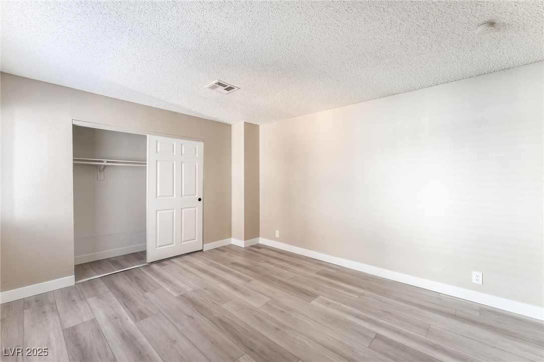 3151 North Soaring Gulls Drive, Unit 1188 Las Vegas, NV 89128 - Photo 21 of 43 Unfurnished bedroom with a closet, light wood-style floors, and a textured ceiling