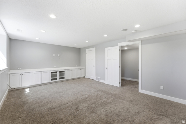 1614 Aspen Loop Provo, UT 84606 - Photo 28 of 47 Spacious room featuring light gray walls, recessed lighting, wall-to-wall carpeting, and an extensive built-in media console with white cabinetry and display shelving
